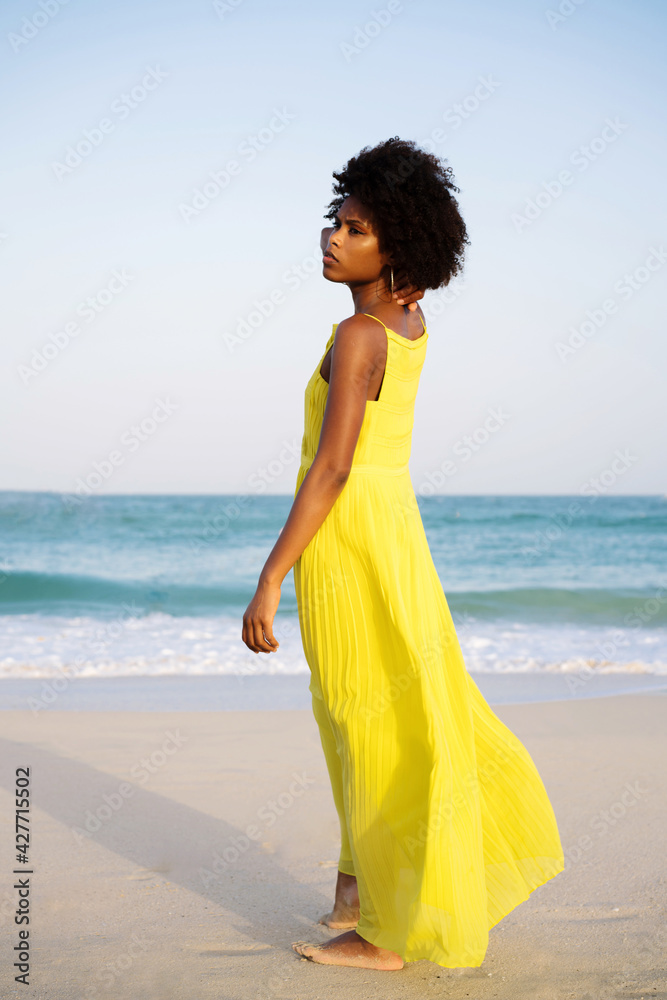 Low angle shot beautiful black woman with afro wearing yellow dress against blue sky