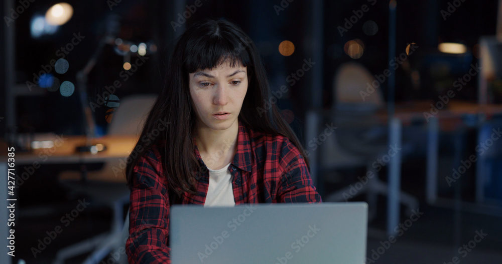 Young Emotional Caucasian Woman Executive Working Late at Office Communicating on Laptop Typing Messages on Social Media. Casual Lifestyle. Young Emotional Caucasian Woman Executive Working Late at Office Communicating on Laptop Typing Messages on Social Media. Casual Lifestyle.