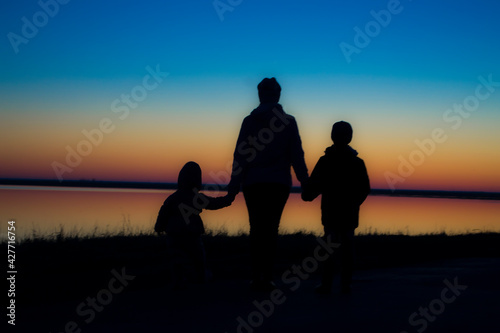 Mother and children hold hands in the background of the sunset.