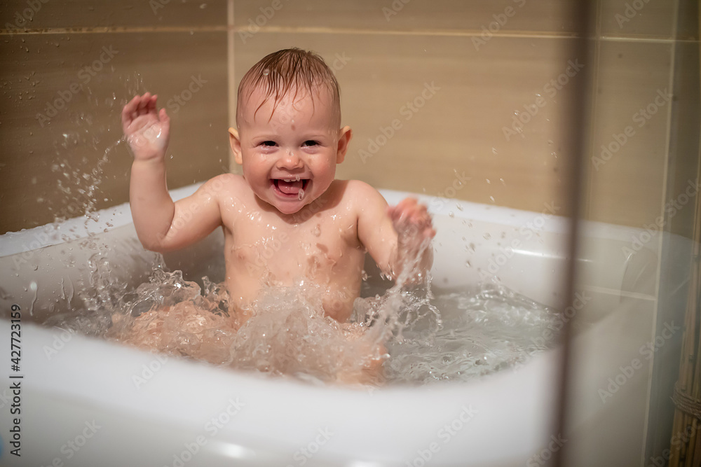 Little charming girl babe plays in the water in small inflatable baby pool located in the shower stall in bathroom, baby girl smiling and having fun Little charming girl babe plays in the water in small inflatable baby pool located in the shower stall in bathroom, baby girl smiling and having fun