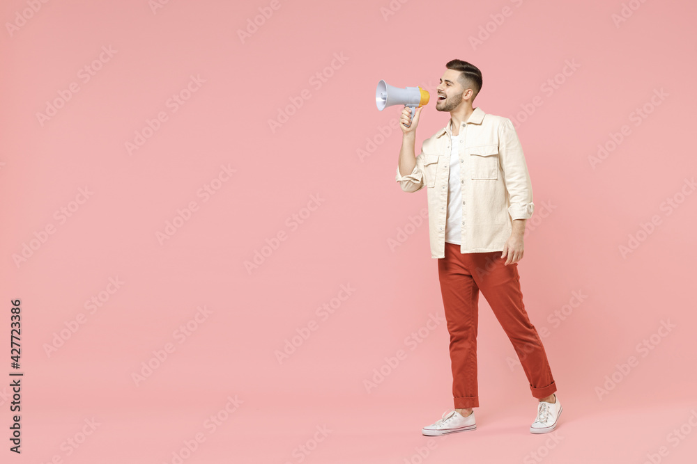 Full length side view young successful happy fun fashionable smiling caucasian man 20s in jacket white t-shirt screaming shout in megaphone hot news isolated on pastel pink color background studio. Full length side view young successful happy fun fashionable smiling caucasian man 20s in jacket white t-shirt screaming shout in megaphone hot news isolated on pastel pink color background studio.
