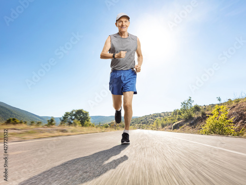 Elderly man jogging on an asphalt road on a sunny day