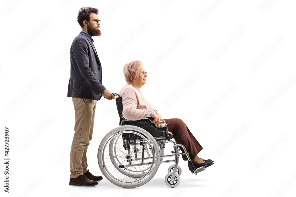 Full length profile shot of a bearded man pushing an elderly lady seated in a wheelchair Full length profile shot of a bearded man pushing an elderly lady seated in a wheelchair