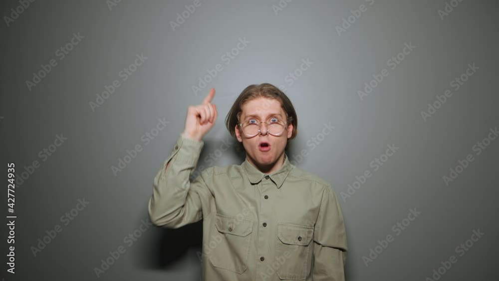 Pensive funny student in glasses and a shirt looks up and thinks and finds an idea with a smile on his face and raises his finger. Pensive funny student in glasses and a shirt looks up and thinks and finds an idea with a smile on his face and raises his finger.