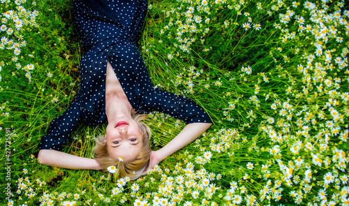 Above view at blonde woman in black dress lying in countryside chamomiles flowers meadow