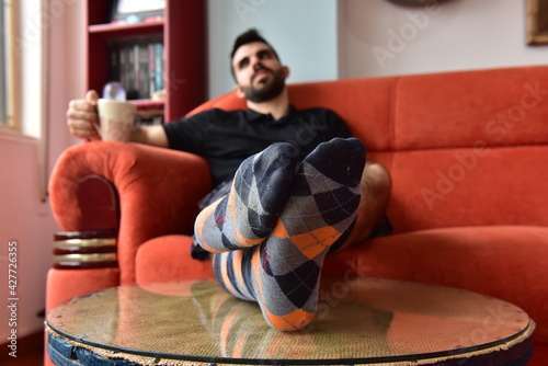 Boy in socks sitting on the sofa holding cup of coffee.
