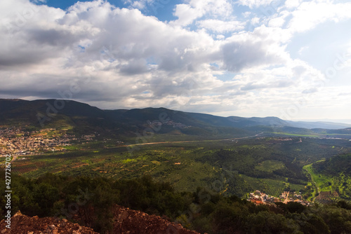 A view of a mountain range and a green valley in the morning at sunrise  against a dramatic backdrop of blue skies and clouds. North District Israel. High quality photo. Travel concept hiking