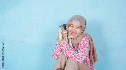 portrait of the asian hijab woman with cat on the color background - free copy space for text © Rizky