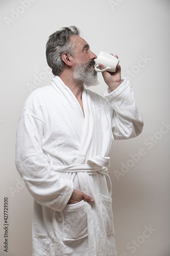 older man with beard drinking coffee in bathrobe