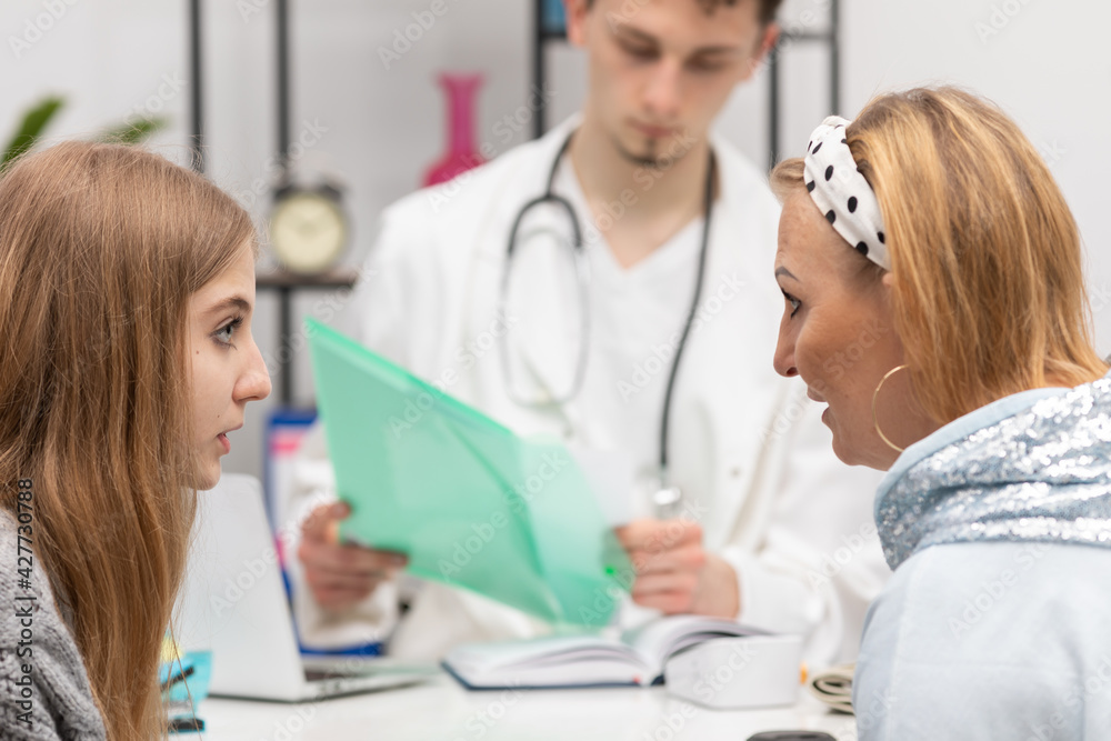 A mother and daughter are talking in a doctor's office about an illness the doctor has pointed out. The primary care physician A mother and daughter are talking in a doctor's office about an illness the doctor has pointed out. The primary care physician