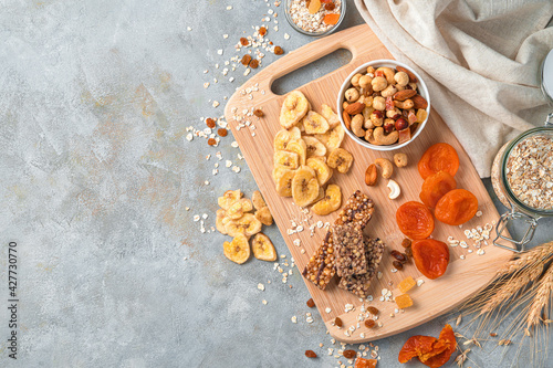 Vitamin-rich, healthy natural sweets on a gray background. Granola bar, nuts and dried fruits on a wooden board.