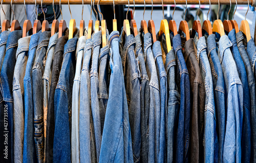 A lot of jeans jackets hanging on a hanger in the store. A row of jeans jackets in the store. Sale of jeans in the store on the counter. Texture of jeans