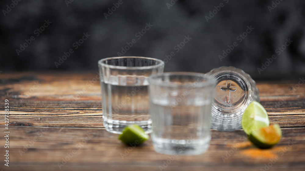 Bebida mexicana de agave mezcal tipo tequila hecha en oaxaca servida en veladora oaxaqueña sobre mesa de madera rústica acompañada de limón y sal de gusano Bebida mexicana de agave mezcal tipo tequila hecha en oaxaca servida en veladora oaxaqueña sobre mesa de madera rústica acompañada de limón y sal de gusano