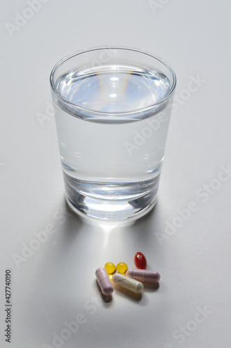 a glass of drinking water and several capsules with vitamins. light background. close-up.