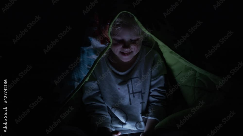 Little girl uses her cell phone at night under the blankets. Little girl uses her cell phone at night under the blankets.