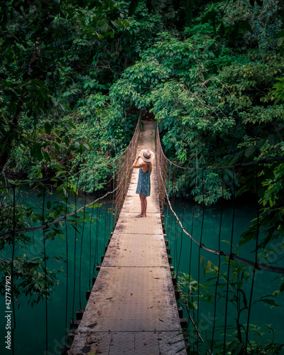 Fototapeta Naklejka Na Ścianę i Meble -  Woman walking on suspension bridge over green colored river