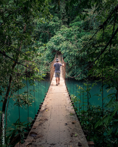 Man walking on suspension bridge over green colored river