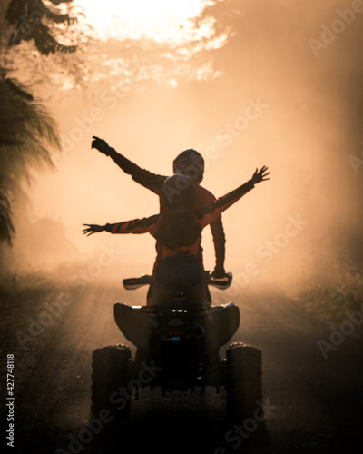 Silhouette of friends driving quad bike at sunset