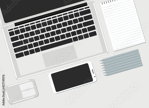 On the desktop are a laptop, a mobile phone and a paper notebook. View from above