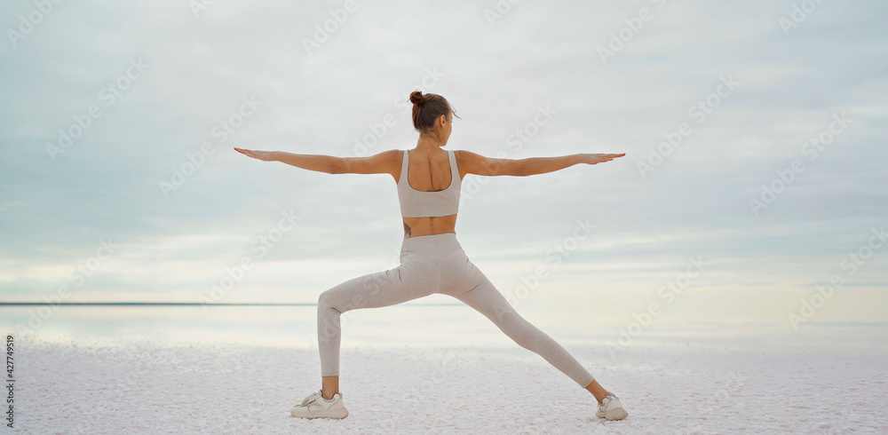 Rear view athletic woman doing yoga, body stretch outdoors on salt coast lake - obrazy, fototapety, plakaty 