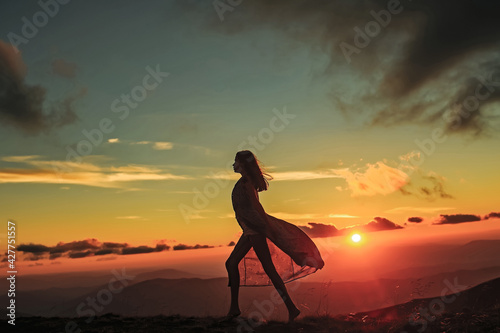 Woman walking at beautiful view on sunset or sunrise in blue sky with clouds. Silhouette on natural background.