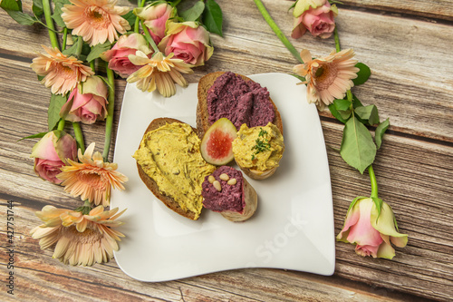 Close-up of a delicious breaktfast with bread and parfait, humus and fruits in a lovely arrangements with flowers on a wooden background