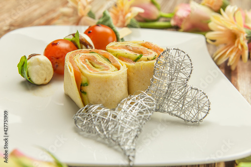 Close-up of a gourmet dinner with salmon rolls, tomatoes and mozarella cheese in a lovely arrangement with flowers on a wooden background	 photo