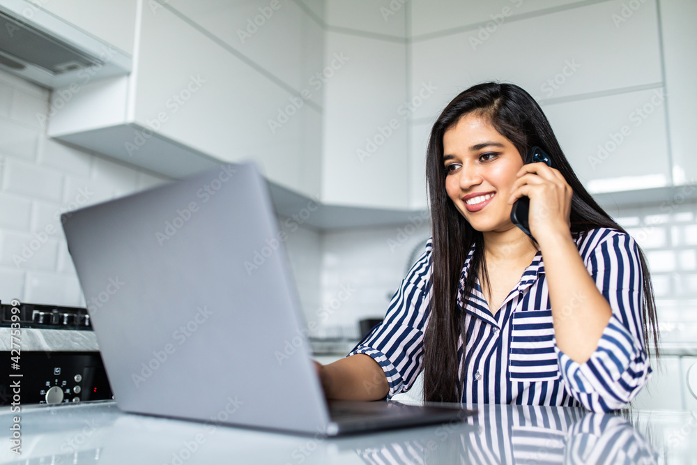 Happy young woman at home, talking on mobile phone and using laptop Happy young woman at home, talking on mobile phone and using laptop