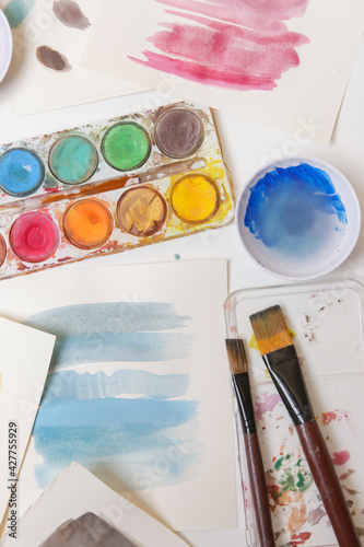 Watercolor paints palette, brushes and papers on table. Creative hobby or art therapy concept.