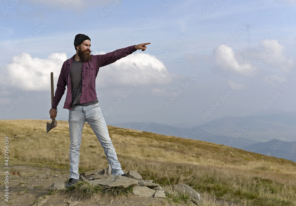 Man with ax on mountain. Carefree happiness freedom concept. Hipster man with beard and moustache in hat jumps with axe on mountain top on cloudy sky. Man with ax on mountain. Carefree happiness freedom concept. Hipster man with beard and moustache in hat jumps with axe on mountain top on cloudy sky.