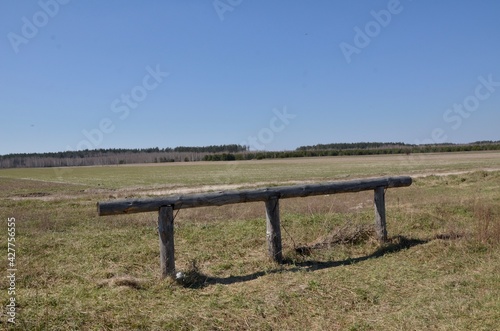 Broken wooden fence on the field against the background of the forest. Beautiful landscape in the spring sun.