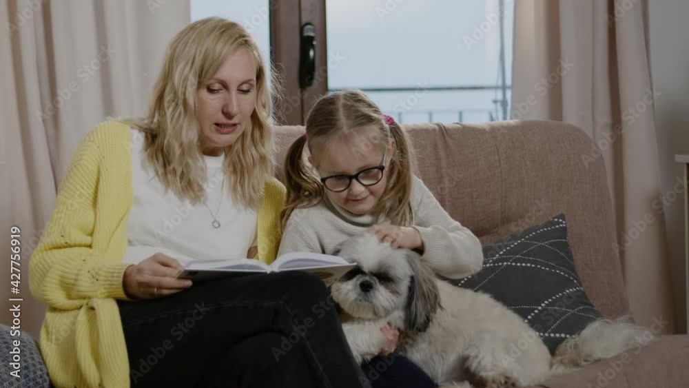 Mom read daughter book while girl is stroking cute dog lying on knees Rbbro. Mother and daughter Mom read daughter book while girl is stroking cute dog lying on knees Rbbro. Mother and daughter