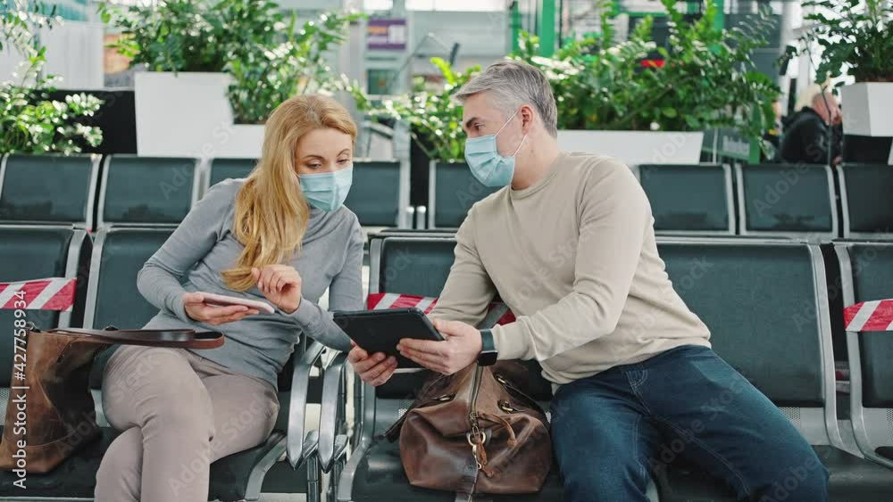 Mature man asking for help with gadget from woman sitting through one seat, both wearing protective medical masks Mature man asking for help with gadget from woman sitting through one seat, both wearing protective medical masks