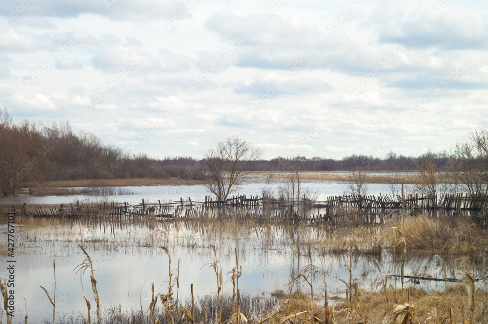 April cloudy landscape in flood of the river. Spring flood. Flooding meadows farms yard fence and gardens underwater April cloudy landscape in flood of the river. Spring flood. Flooding meadows farms yard fence and gardens underwater