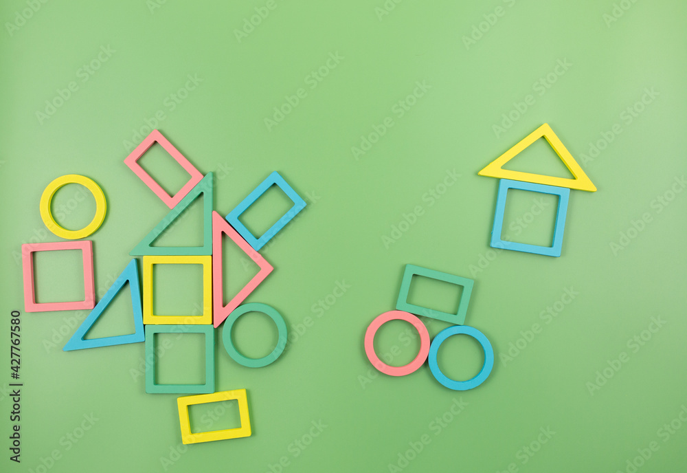 Multicolored wooden blocks on a green background. Trendy puzzle toys. Geometric shapes: square, circle, triangle, rectangle. Educational toys for kindergarten, preschool, or daycare. Back to school Multicolored wooden blocks on a green background. Trendy puzzle toys. Geometric shapes: square, circle, triangle, rectangle. Educational toys for kindergarten, preschool, or daycare. Back to school
