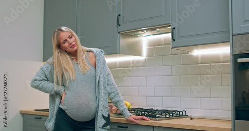 A pregnant woman begins to experience labor contractions while standing in the kitchen.