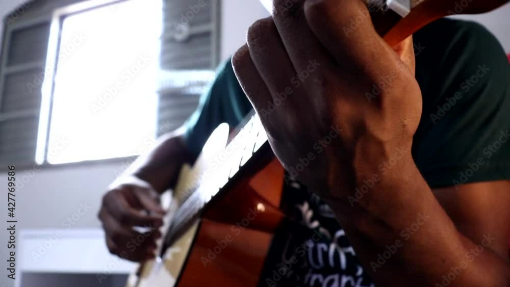 Homem negro tocando violão, ângulo da câmera contra plongée.