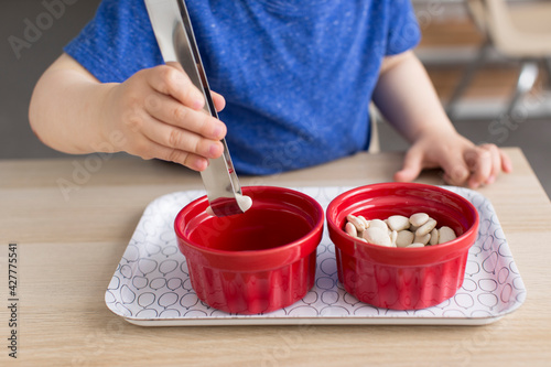 фотографія Little boy transferring beans into ceramic dishes while practicing practical lif