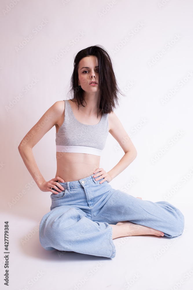 woman in blue jeans and sports top sits, white studio background woman in blue jeans and sports top sits, white studio background