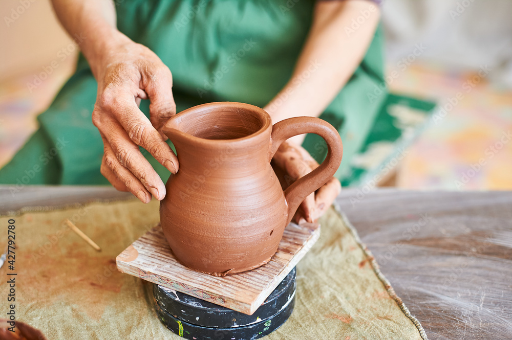 potter woman's hands in a green apron demonstrate a clay jug she has made