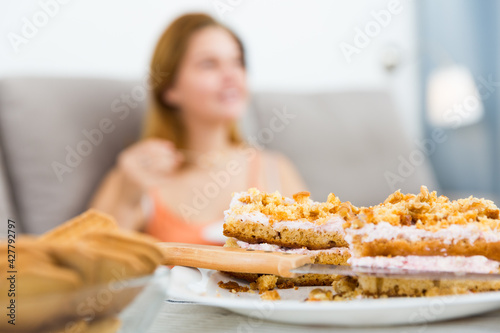 Positive woman sitting on sofa with plate with fresh cake