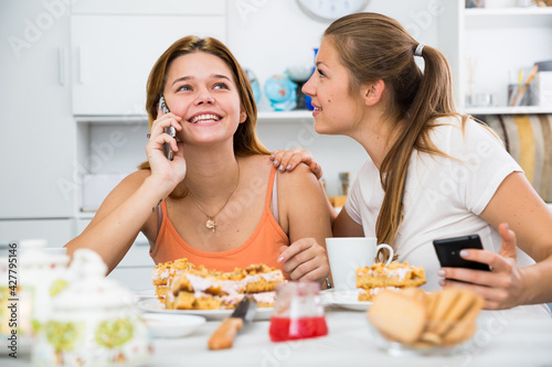 Slika na platnu Girlfriends are playfull talking by phone at home.