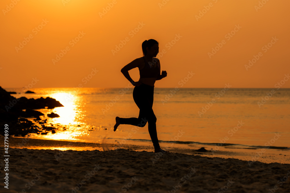 Silhouette athletic woman jogging exercise and relax and freedom on sand beach. People running and workout in sunset background