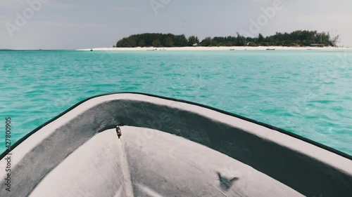 An African boat sails across the turquoise ocean towards Mnemba Island, Zanzibar. Walk on a fishing boat to a tropical island. View of the bow of the boat. Tanzania, Africa. photo
