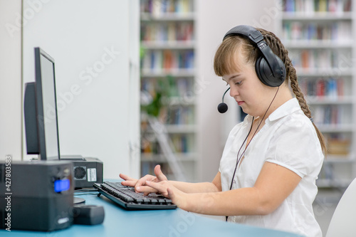 Young girl with syndrome down uses computer at library. Education for disabled children concept photo