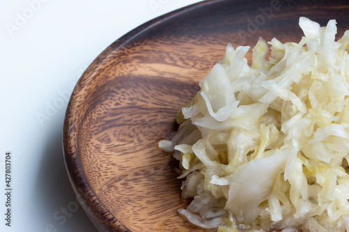 Closeup of sauerkraut on a wood plate isolated on a white background. Sauerkraut is finely cut raw cabbage that has been fermented by various lactic acid bacteria. photo