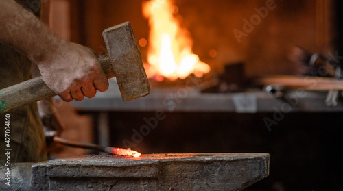 Close up blacksmith working metal detail with hammer on the anvil in rustic forge. Empty space for text