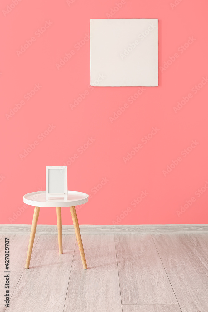 Fototapeta premium Modern table with photo frame near color wall in room