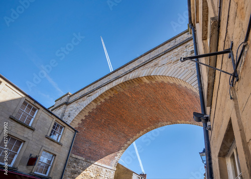 Принти на полотні Jumbo jet aeroplane flying over railway bridge arch viaduct in blue sky with vapour trails