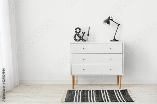 Modern chest of drawers with lamp near light wall in room